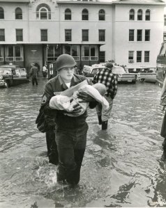 Staff Sergeant Larry Penrod carries newborn baby Garcia along with bottles, records and medication to safety during the evacuation of Salem Memorial Hospital December 23, 1964.